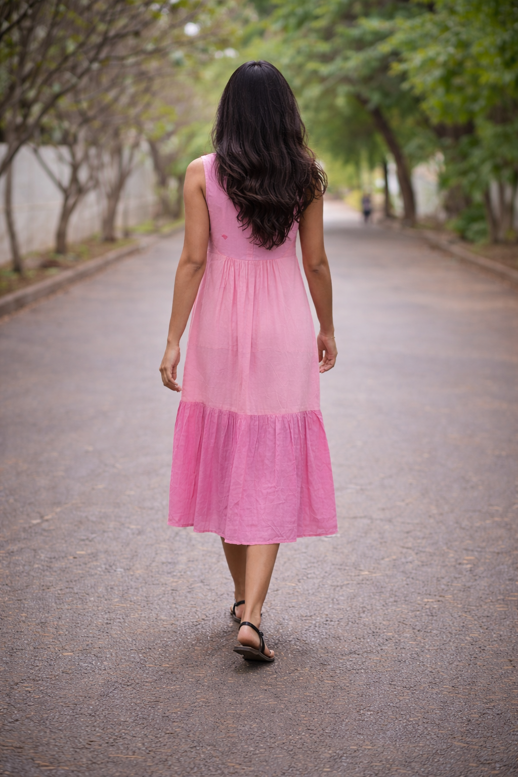 Woman in a pink dress walking down a tree-lined street.